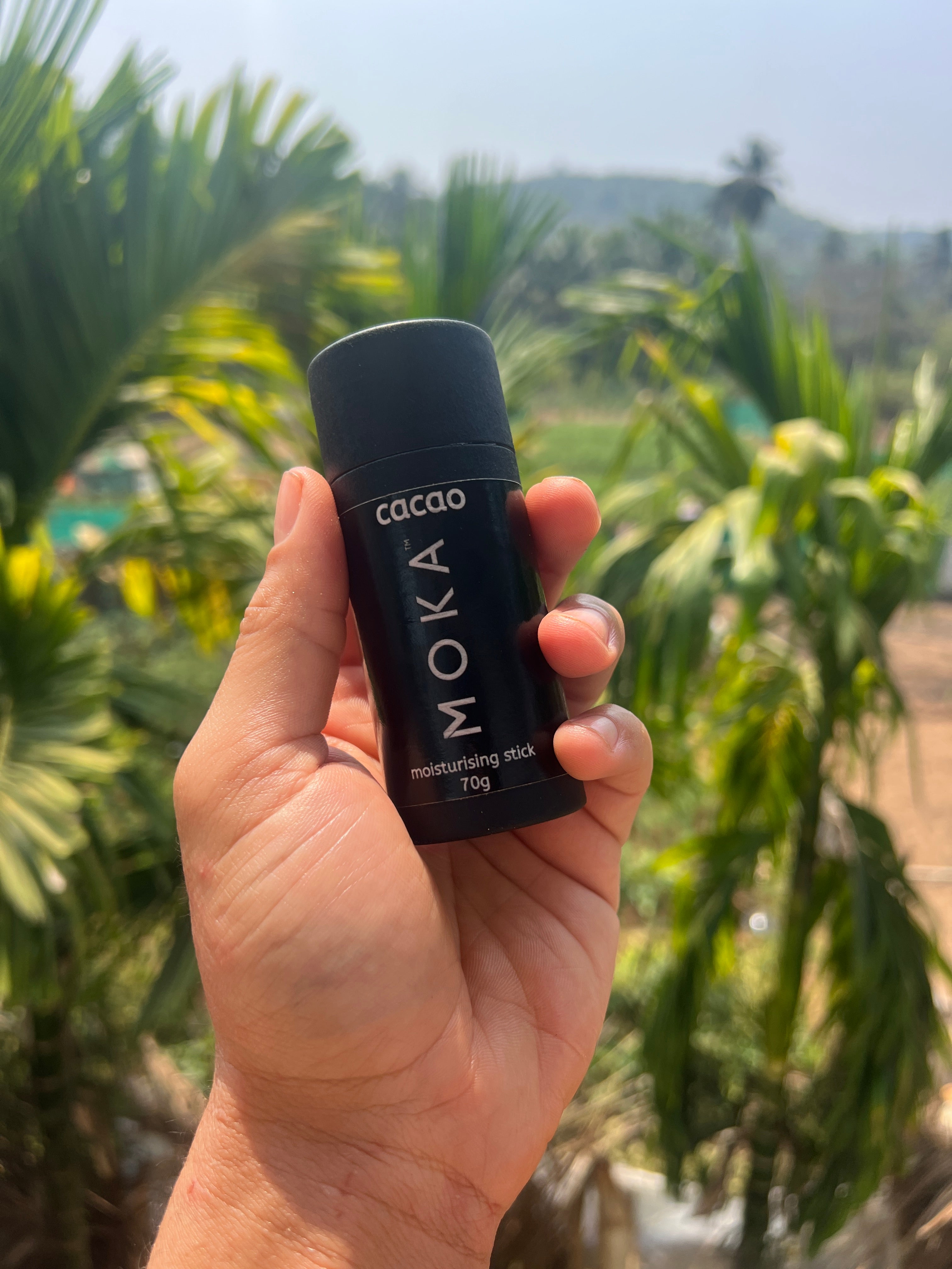 A hand holding the MOKA stick outdoors against jungle greenery